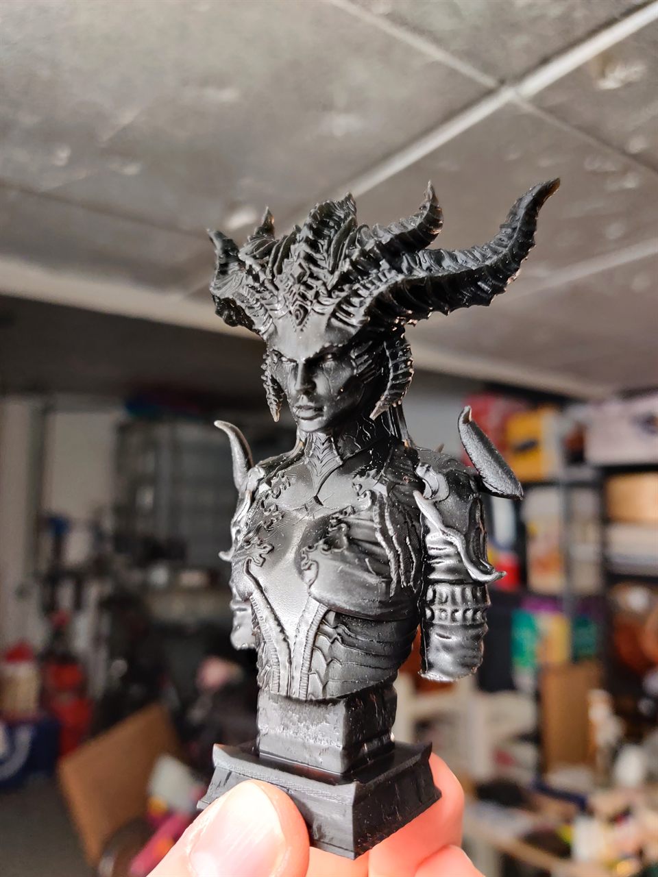Buste imprimé en résine noire tenu entre deux doigts, dans l'atelier